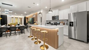 Une cuisine moderne dotée d’un îlot central, d’appareils électroménagers en acier inoxydable et de luminaires suspendus.