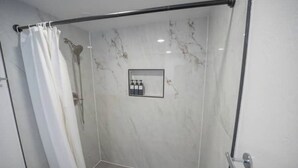 Zona de ducha con mampara de vidrio, alcachofa y un cuadro en la pared.