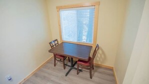 Un coin repas avec une table et des chaises en bois, une fenêtre avec des stores et un plancher de couleur claire.