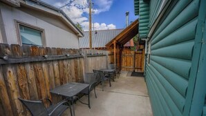 A patio area with a wooden fence, a concrete floor, and metal tables and chairs.