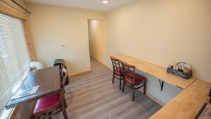 A dining area with a wooden table and chairs, a small kitchen counter, and a window with blinds.