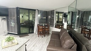 A modern living room with a brown sofa, a dining table with chairs, and a kitchen area with a countertop and a potted plant.