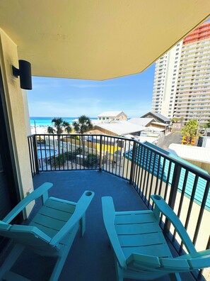 Ein Balkon mit zwei Stühlen, einem Pool und Blick auf Strand und Gebäude.