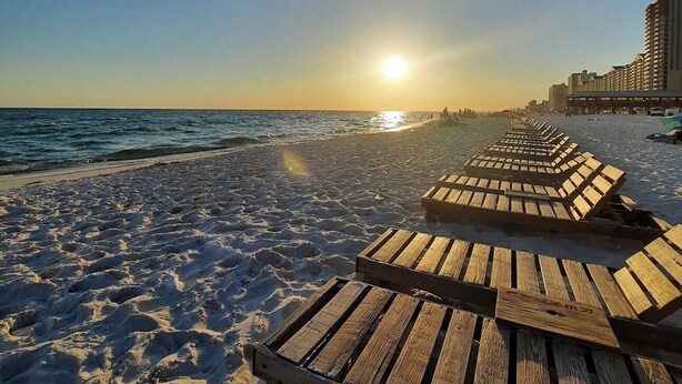 A beach with wooden lounge chairs and a clear sky.