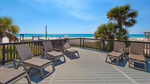 A wooden deck with lounge chairs overlooking a beach.