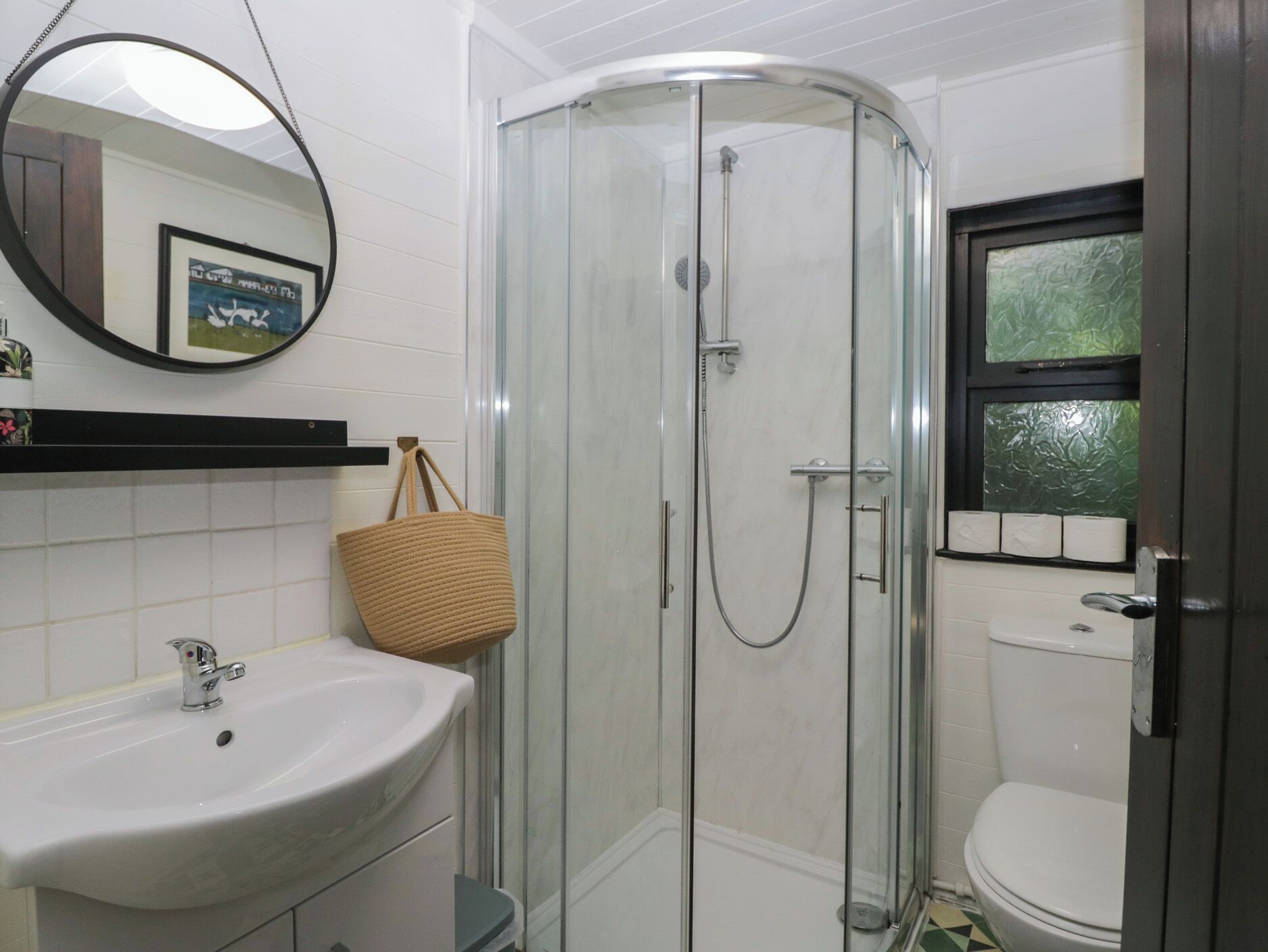 A bathroom with a glass-enclosed shower, a white sink, a mirror, and a toilet.
