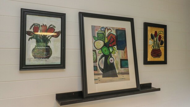 Three framed artworks on a wall, each depicting vases with flowers.