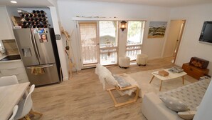 Un salon moderne comprenant un canapé, une table basse et un coin repas avec une table et des chaises. On y trouve également une cuisine équipée d’un réfrigérateur et de bouteilles de vin.