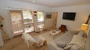 Un salon comprenant un canapé, un fauteuil, une table basse et un téléviseur. Une porte-fenêtre coulissante donne accès à un espace extérieur.