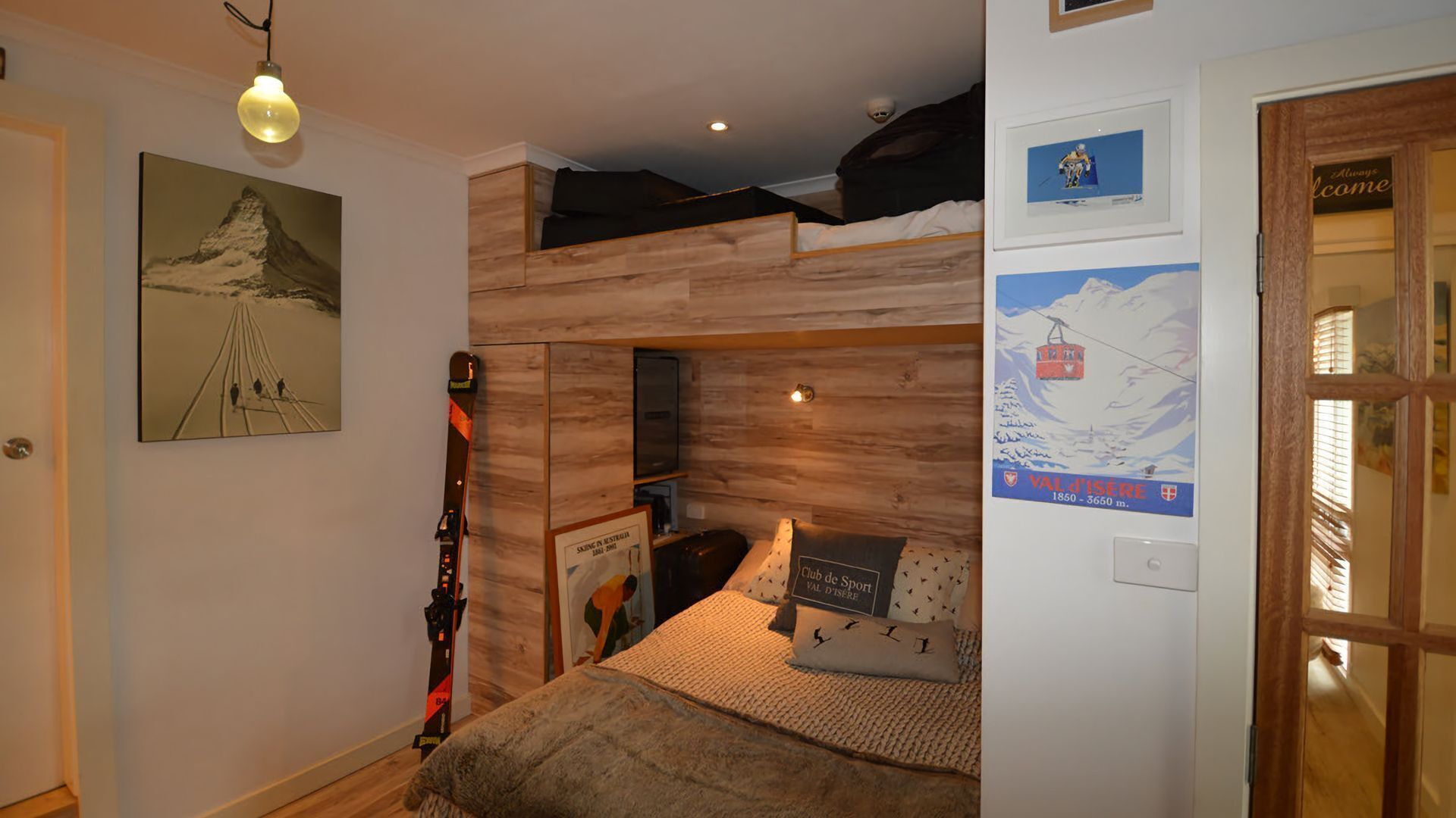 A room with a bunk bed, wooden wall paneling, a ski lift poster, and a ski slope painting.