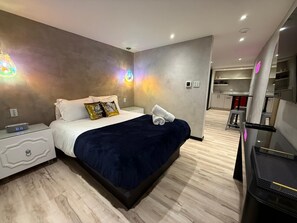 A modern hotel room with a large bed, a nightstand with a digital clock, and a bathroom visible in the background. - Stay @La Placita with us and dive into Puerto Rico's #1 cultural hotspot. (San Juan)