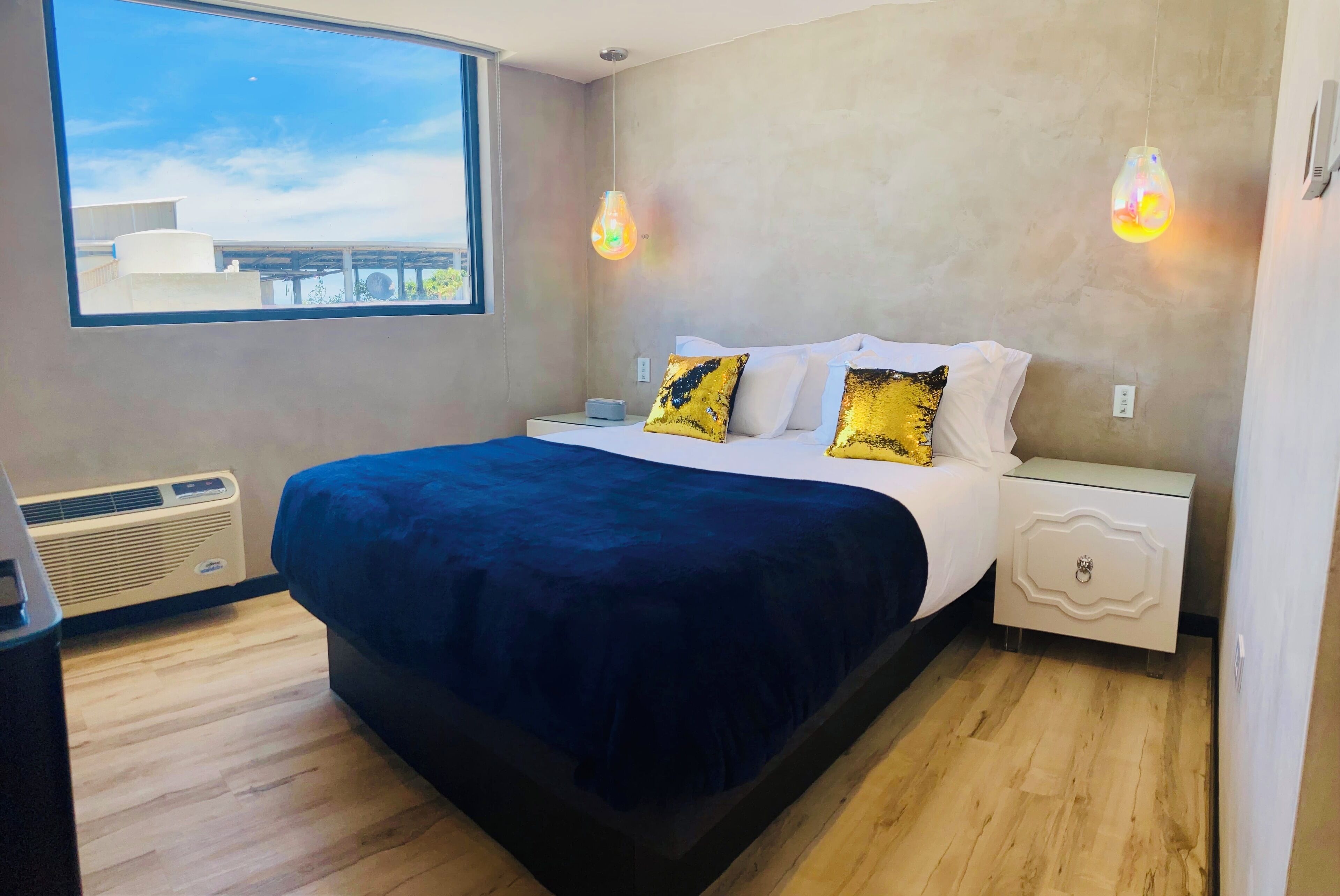A bedroom with a large bed, a nightstand, a bedside table, a window, and a view of the outside.