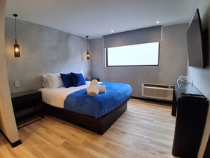 Ein modernes Schlafzimmer mit einem großen Bett, einem Flachbildfernseher und einem Fenster mit Tageslicht.