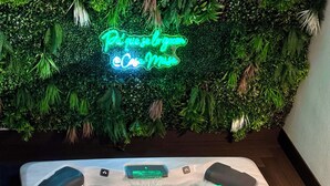 A hot tub with a neon sign in the background, surrounded by lush greenery.