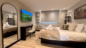 A modern bedroom with a large bed, a desk, a chair, a TV, and a mirror.