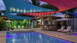 Una piscina con zona de bar, tumbonas y un área de estar al aire libre con sombra.