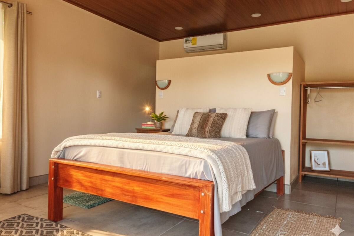 Une chambre à coucher avec un lit en bois, des murs de couleur beige et un ventilateur de plafond.
