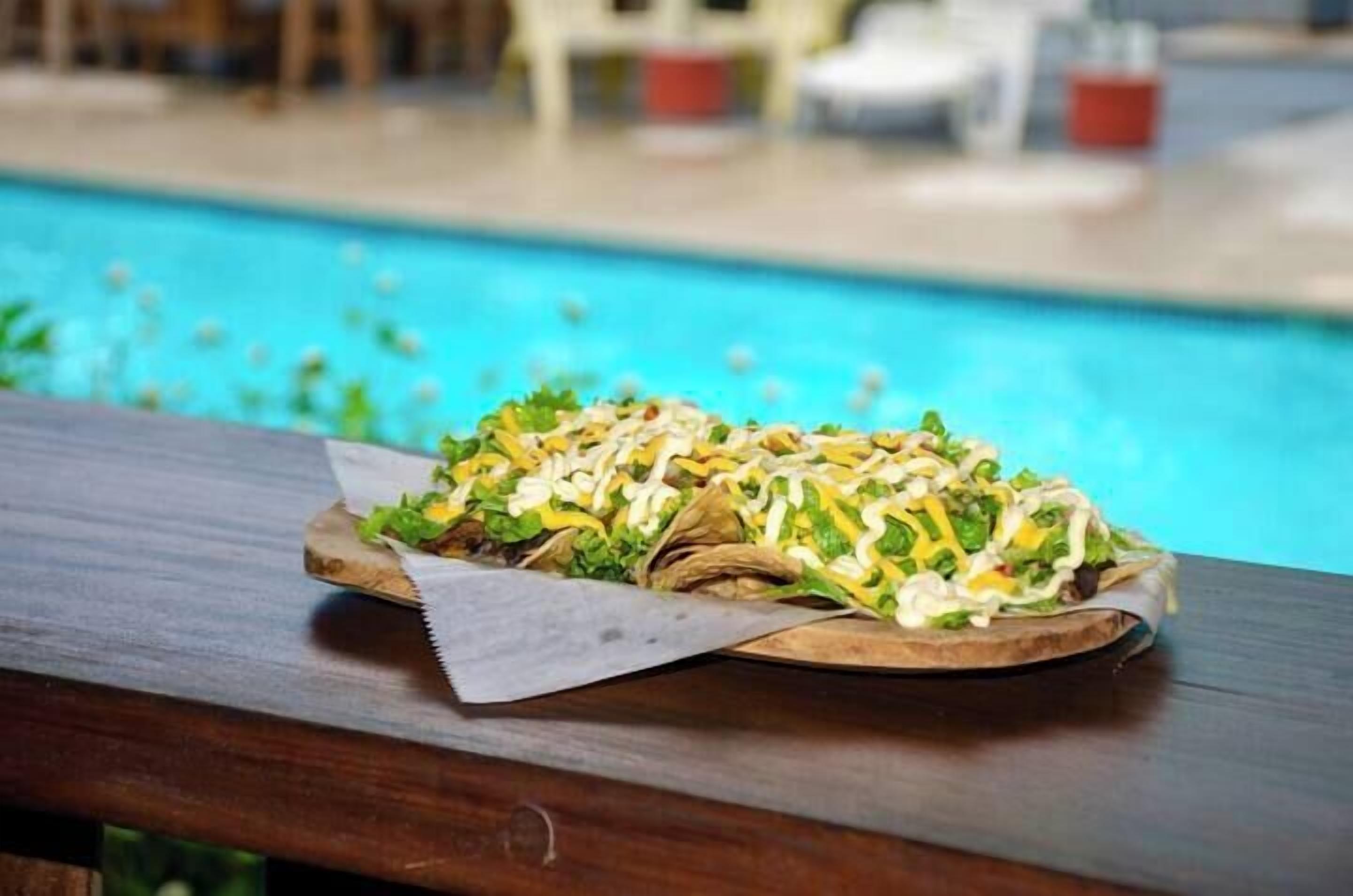 A wooden table with a wrapped food item, possibly a wrap, near a poolside area.