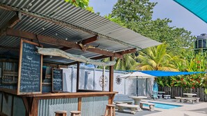 Un espacio de estar rústico al aire libre con piscina, taburetes de madera y un menú en una pizarra.