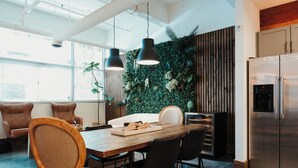 Une cuisine moderne avec un coin repas, comprenant une table en bois, des chaises noires, un réfrigérateur en acier inoxydable et un mur végétal vertical vert.