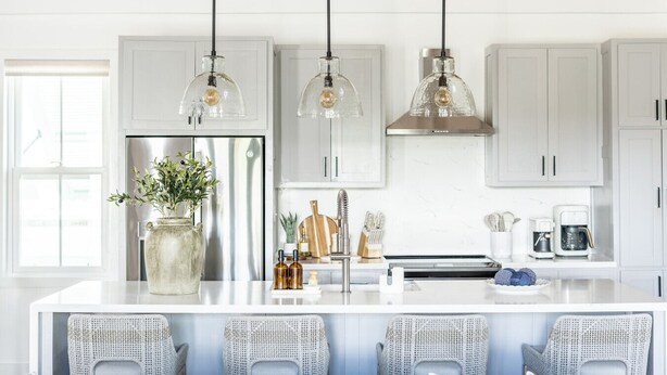 Une cuisine moderne avec des armoires blanches, un réfrigérateur en acier inoxydable, un grand îlot central doté de tabourets, des luminaires suspendus et un plafond en bois.