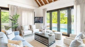 Un salon spacieux doté d’une grande fenêtre, d’un téléviseur à écran plat et donnant sur une piscine.