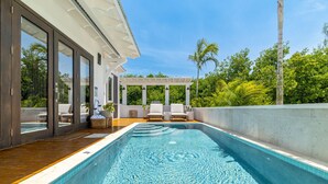 Une piscine extérieure moderne, avec une eau d’un bleu limpide, entourée d’une terrasse en bois et de chaises longues blanches.