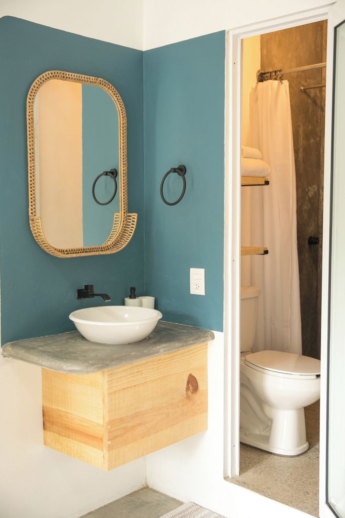 A bathroom with a teal wall, a wooden vanity with a white sink, a mirror with a gold frame, and a shower curtain.