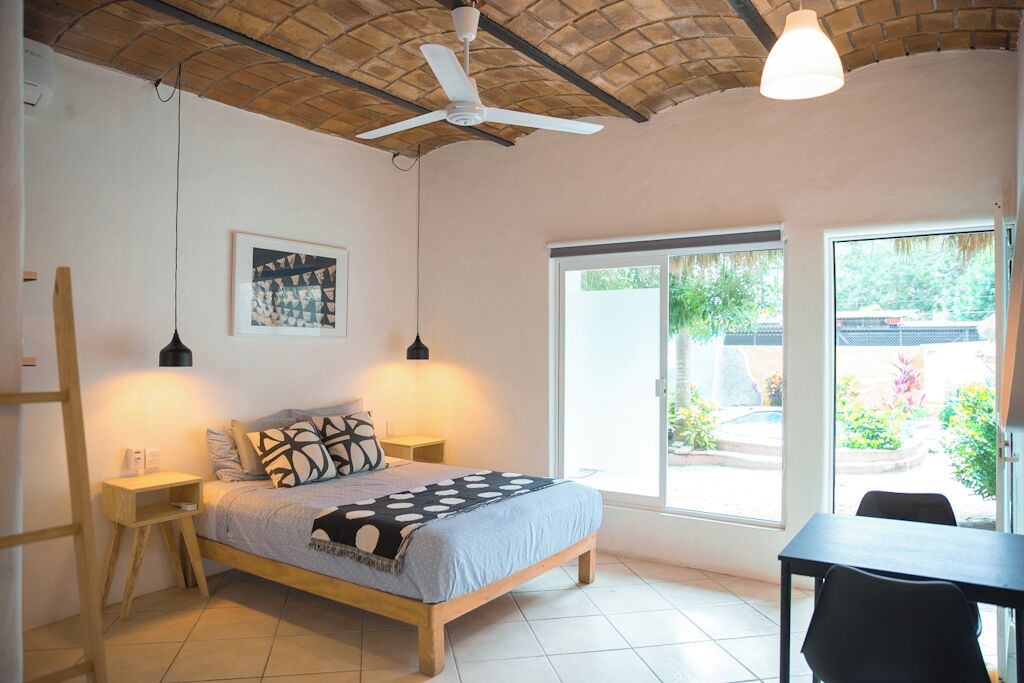Een slaapkamer met een bed, twee nachtkastjes, een plafondventilator, een groot raam en uitzicht op de omgeving.