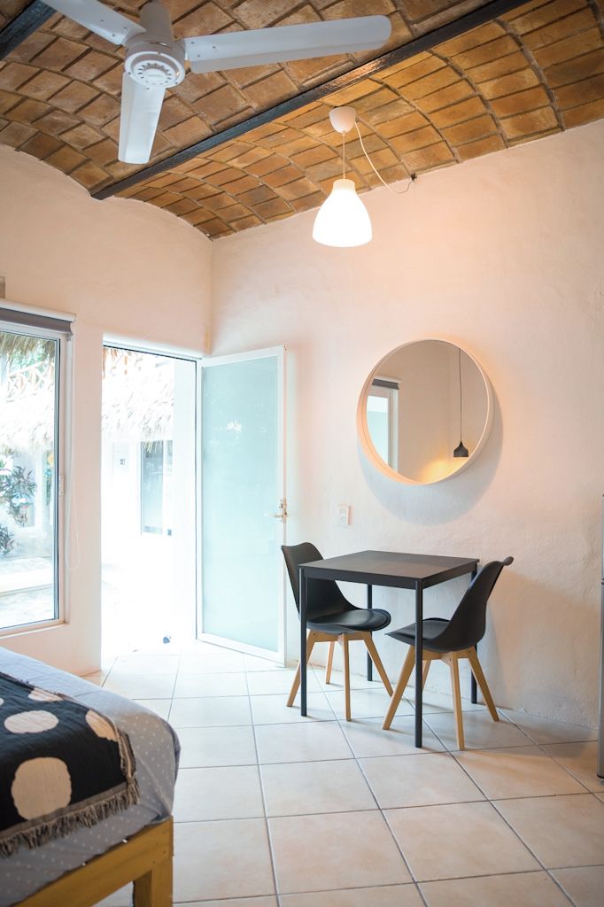 A room with a bed, a dining table with chairs, a ceiling fan, a round mirror, and a door leading outside.