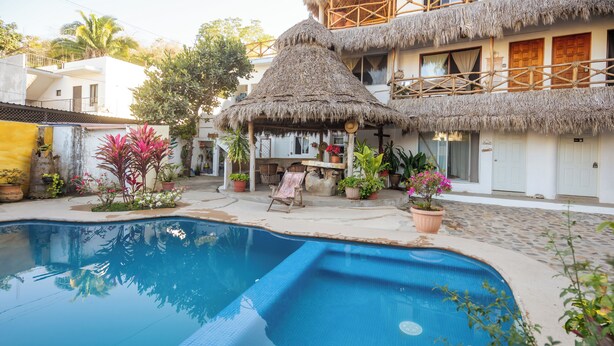 Uma piscina com estrutura de telhado de palha, plantas em vasos e um pequeno espaço de estar ao ar livre.