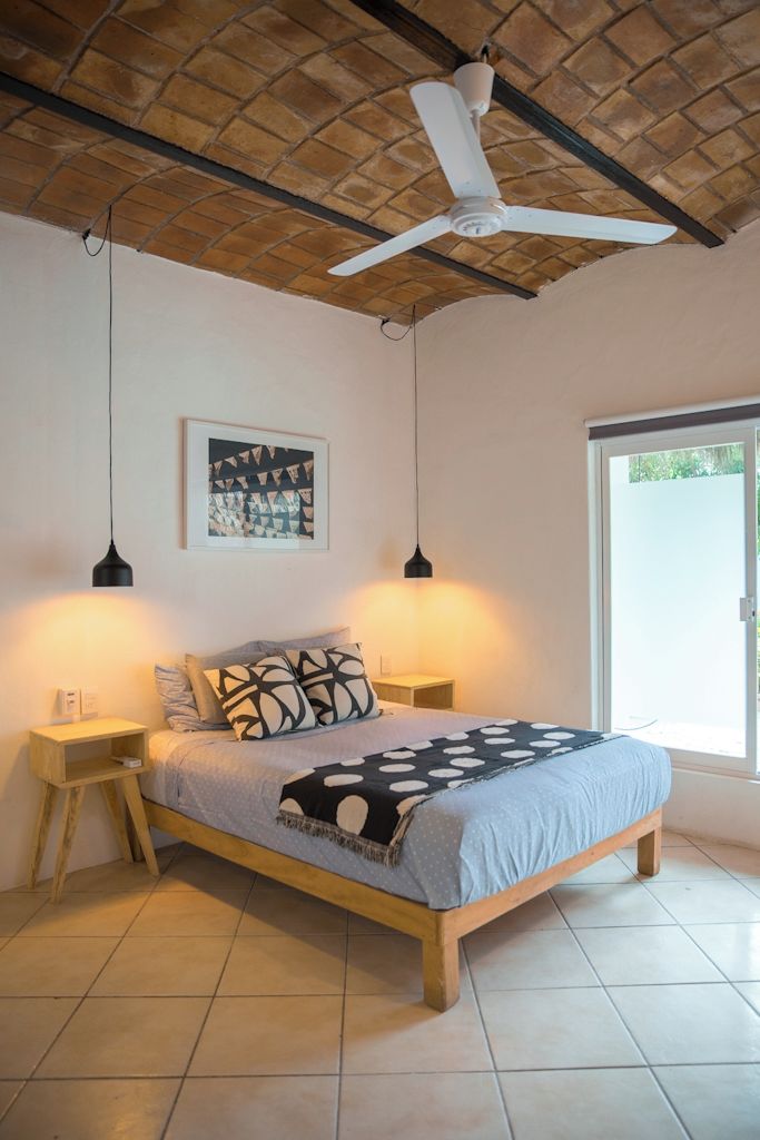 Une chambre à coucher comprenant un lit, deux tables de chevet, un ventilateur de plafond, un tableau accroché au mur et une porte-fenêtre coulissante.