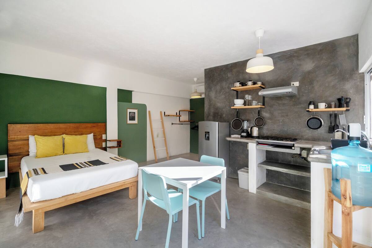 A compact room with a bed, a small dining table, and a kitchenette.