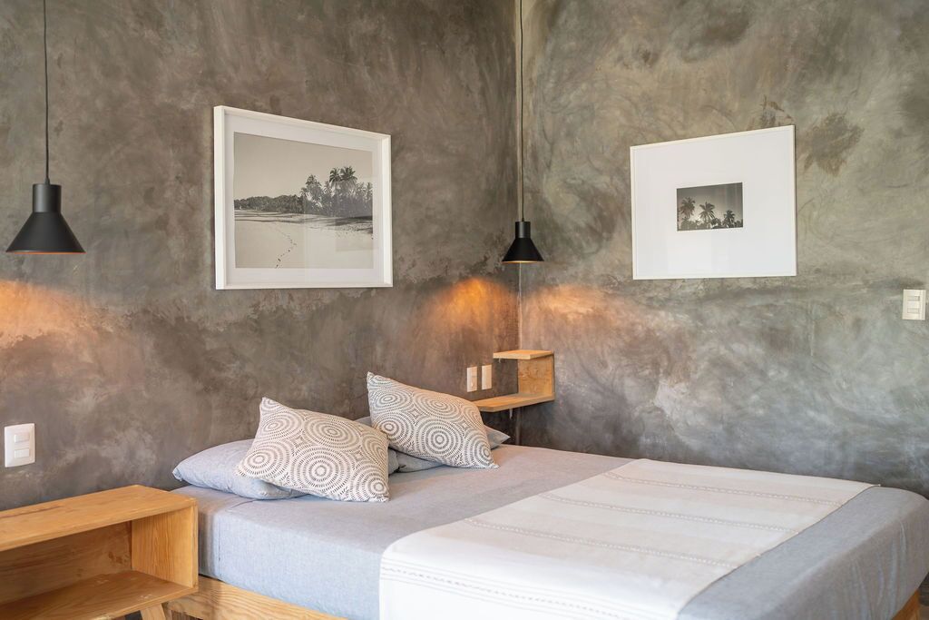 A bedroom with a bed, two pillows, a bedside table, a shelf, and two wall-mounted pictures.