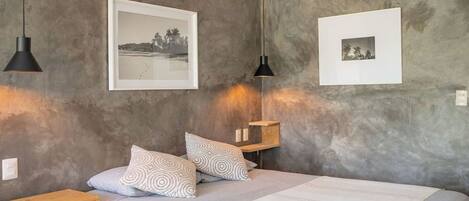 A bedroom with a bed, two pillows, a bedside table, a shelf, and two wall-mounted pictures.