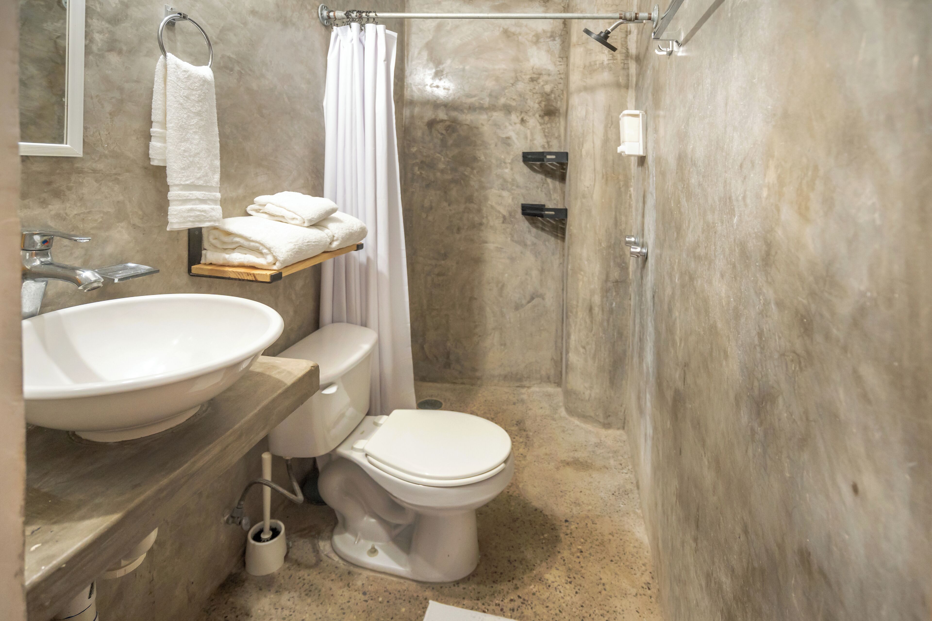 Et badeværelse med stor vask, toilet og bruser. Der er håndklædestang med håndklæder og en hylde med foldede håndklæder.