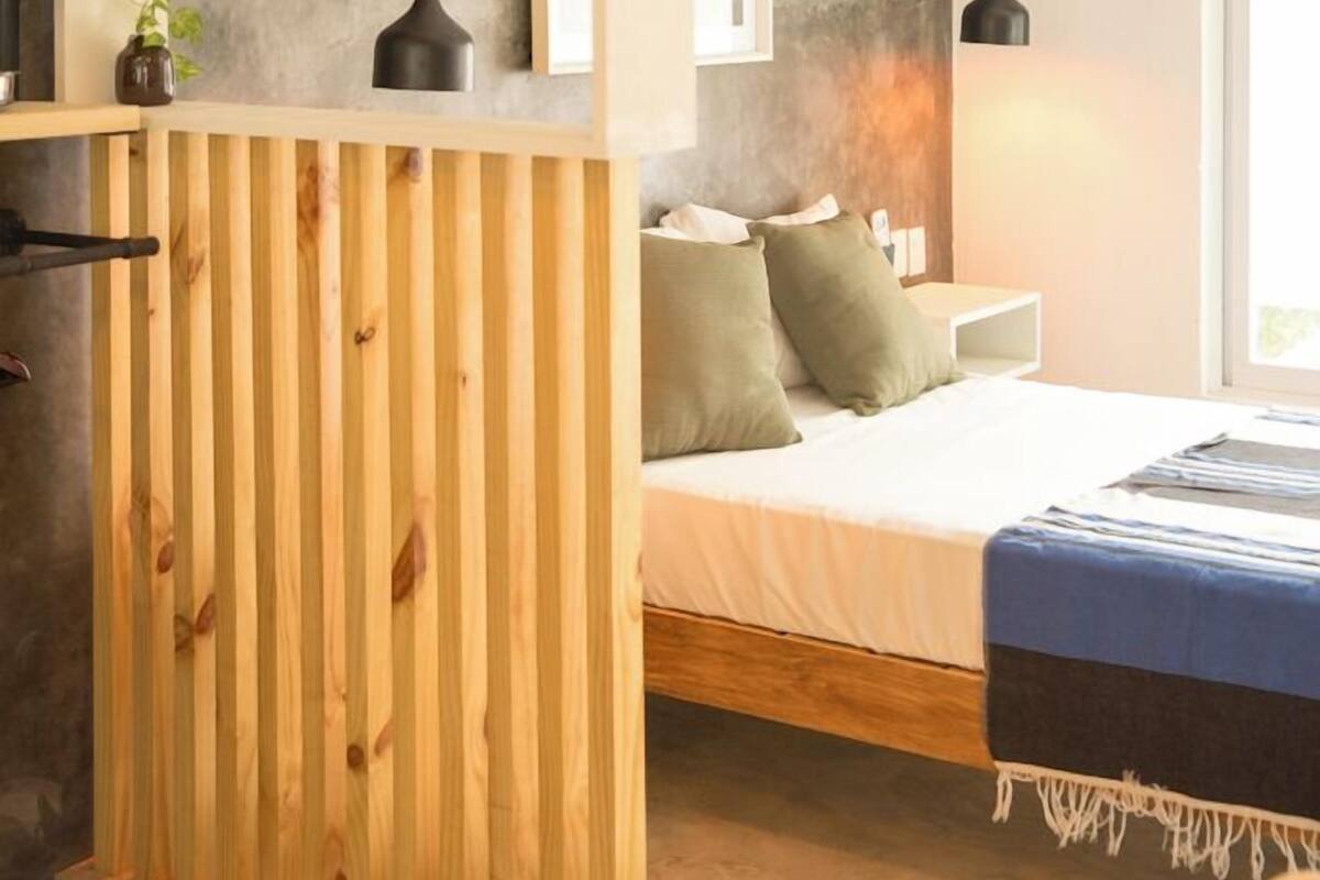 A modern bedroom with a wooden partition, a bed with pillows, a bedside table, and a hanging light fixture.