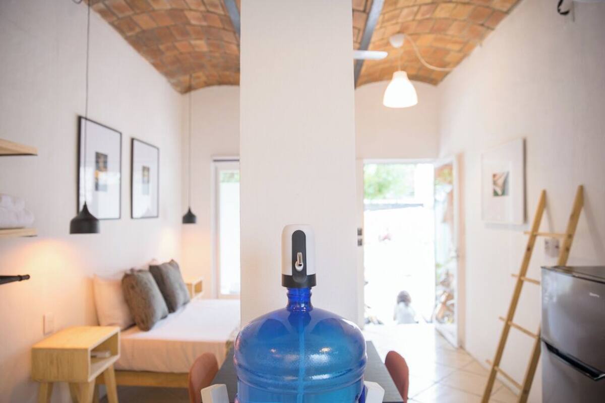 A room with a bed, a large blue water dispenser, a wooden ladder, and a refrigerator.