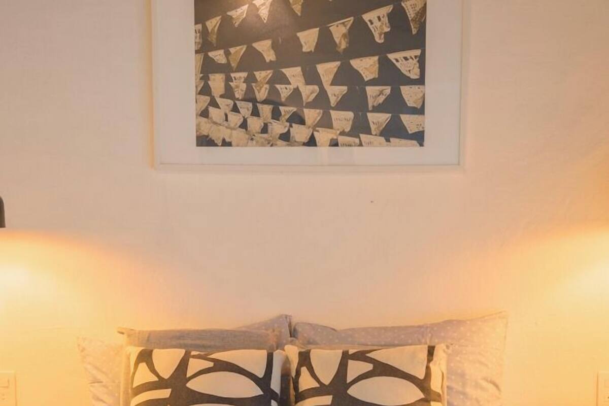 A neatly made bed with patterned pillows and a polka dot blanket, a framed abstract artwork above the bed, and bedside lamps on either side.