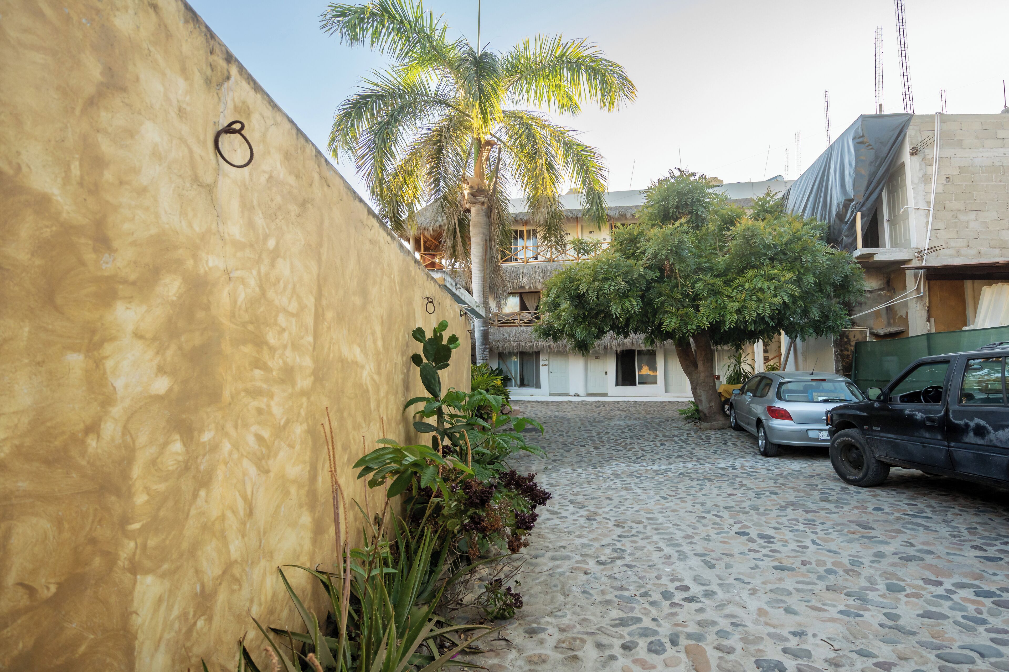 A cobblestone street with a parked car and a building with a thatched roof.