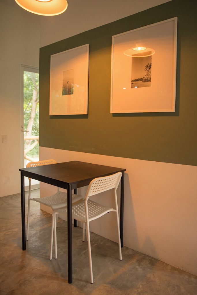 A dining area with a table and two chairs, framed artwork on the wall, and a view of greenery outside.