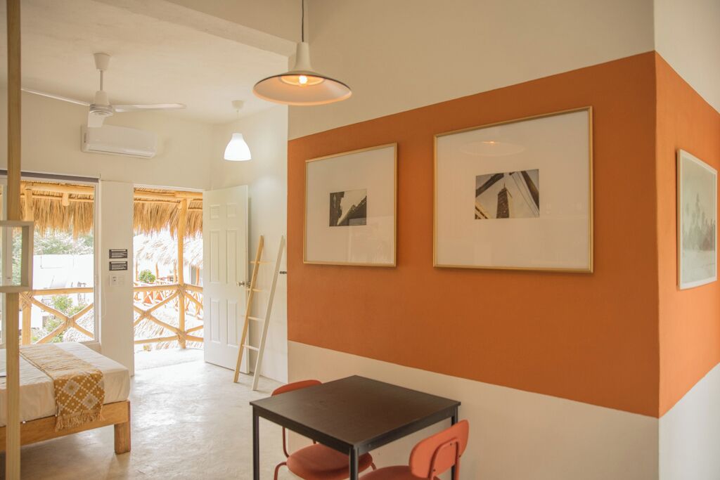 Een kamer met een bed, een tafel met stoelen, ingelijste foto's aan de muur en een plafondventilator.