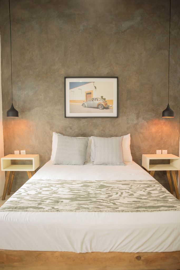 A bedroom with a bed, two bedside tables, a framed picture on the wall, and two pendant lights.