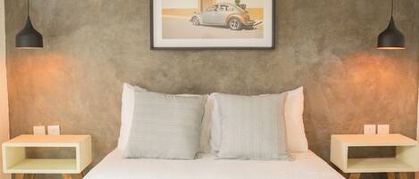 A bedroom with a bed, two bedside tables, a framed picture on the wall, and two pendant lights.