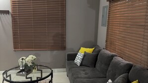 Ein Wohnzimmer mit grauem Sofa, einem Glastisch und einem runden Tisch mit Blumenvase.