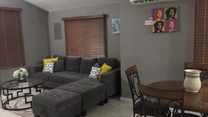Ein Wohnzimmer mit einem Ecksofa, einem Esstisch mit Stühlen und einer Wand-Klimaanlage.