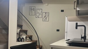 Een moderne keuken met een eethoek, voorzien van een trap, kunst aan de muur en een koffieapparaat.