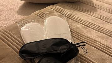 Una cama con cubrecolcha color beige, una almohada blanca y un objeto negro envuelto en plástico transparente.
