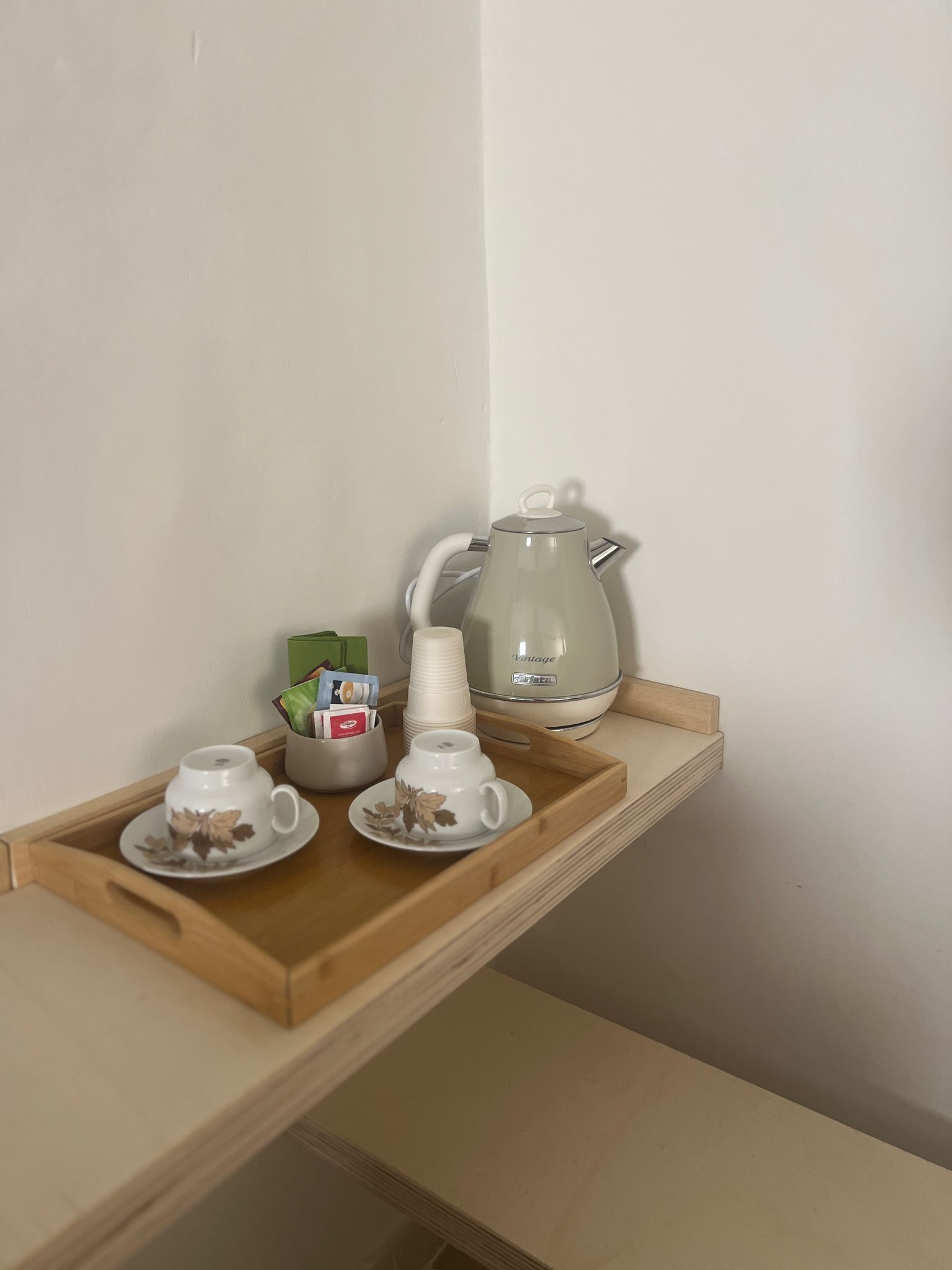Una bandeja de madera con dos tazas y platillos blancos, una tetera blanca y un pequeño recipiente con cartas y una caja verde.