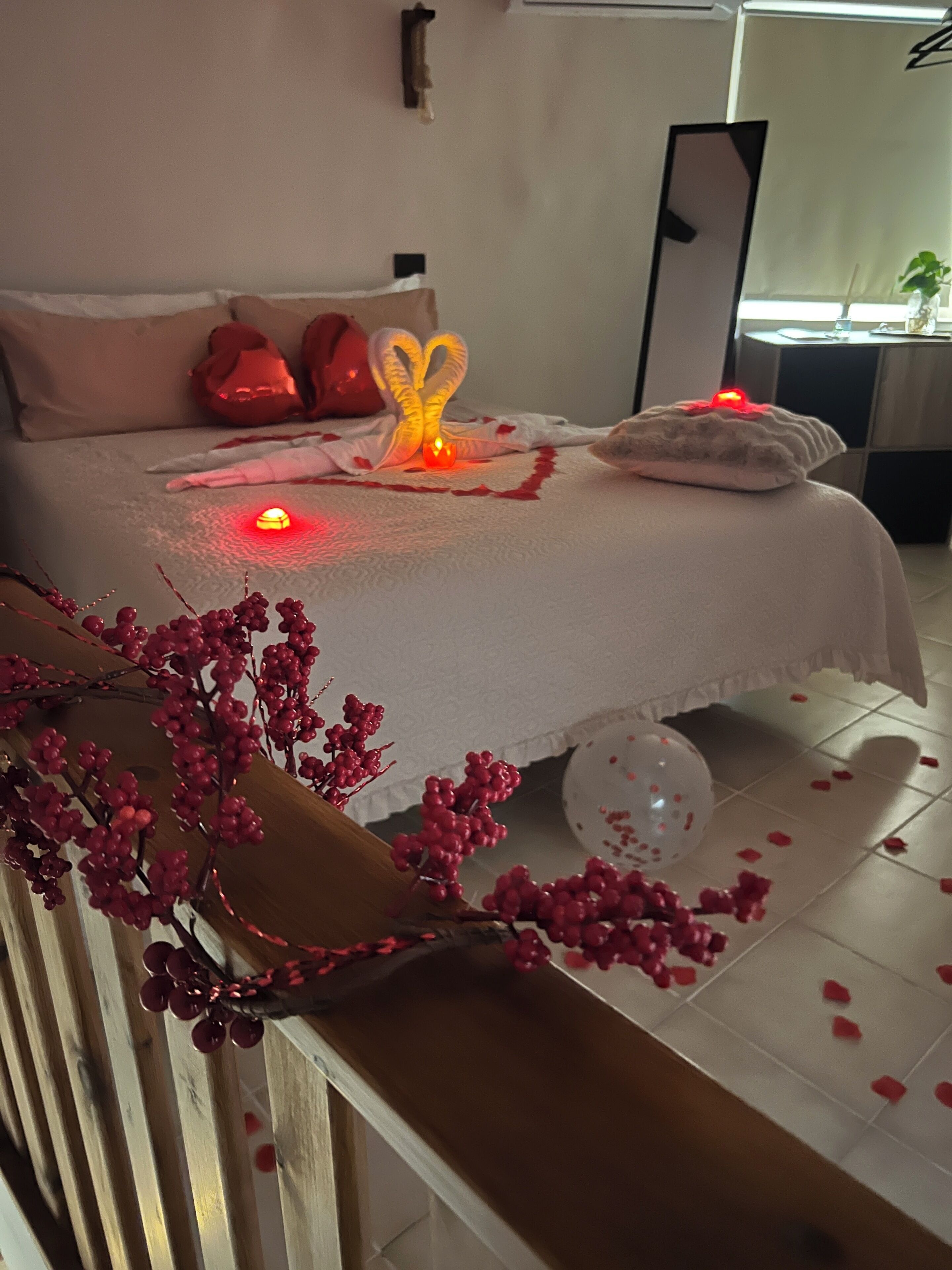 Een netjes opgemaakt slaapkamer met een bed, kussens, een nachtkastje en een spiegel.